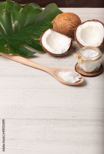 
Bodegón de dos cocos, uno de ellos partido por la mitad con un frasco de aceite de coco y una cuchara de madera con aceite de coco con un espacio vacío debajo para texto.