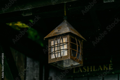 Single vintage lantern hanging over the door to old english cottage house, rusty old electric lamp in shape of a small house hanged above the entrance to a country house. © Gosia
