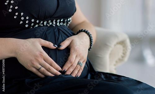 hands female embrace a pregnant belly and show the heart