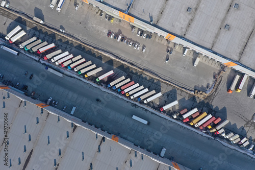 Aerial view of goods warehouse. Logistics center in industrial city zone from above. Aerial view of trucks loading at logistic center. View from drone.