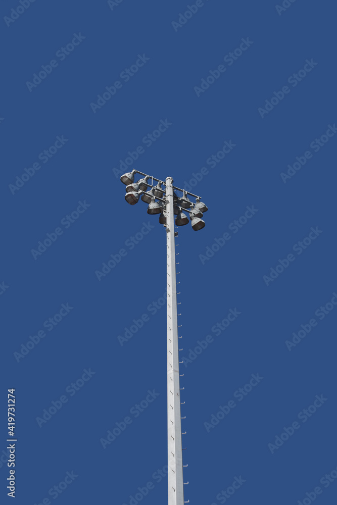 Low angle view of a single very tall mast with sports stadium lights and a bright blue sky behind Low angle view of a single very tall mast with sports stadium lights and a bright blue sky behind