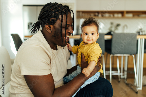 Adorable baby playing with her black dad at home, portrait.