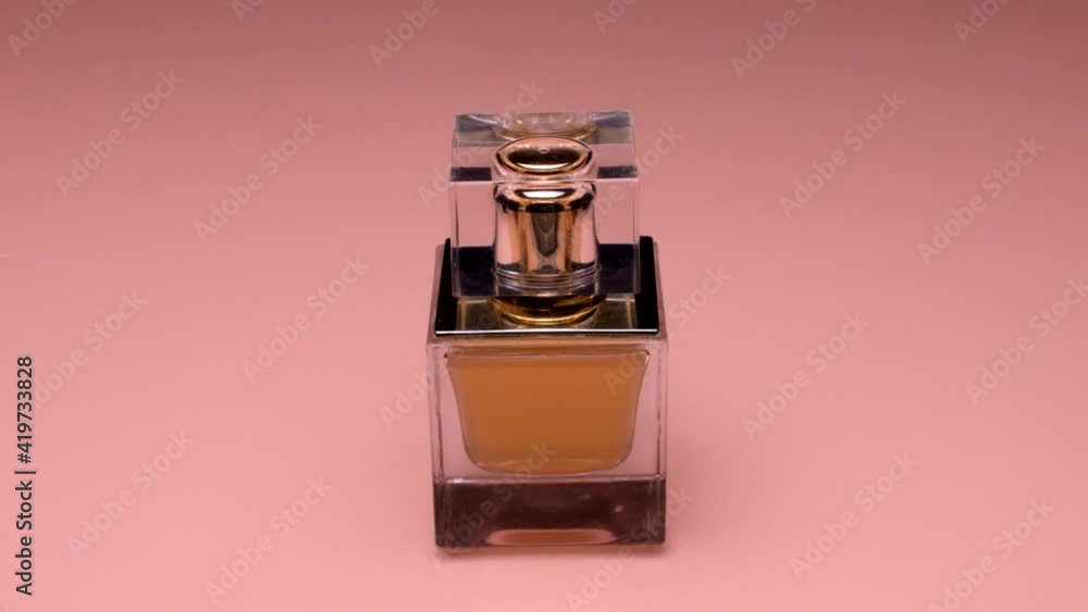 Close-up. The red ribbon wraps around a square bottle of golden perfume and flies away. Perfume on a pink background. Luxury cosmetics Close-up. The red ribbon wraps around a square bottle of golden perfume and flies away. Perfume on a pink background. Luxury cosmetics
