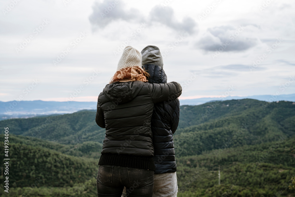 Couple embracing while looking at mountains against sky during winter Couple embracing while looking at mountains against sky during winter
