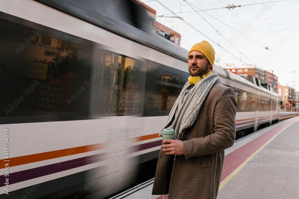 Man with coffee cup looking away while standing on station Man with coffee cup looking away while standing on station