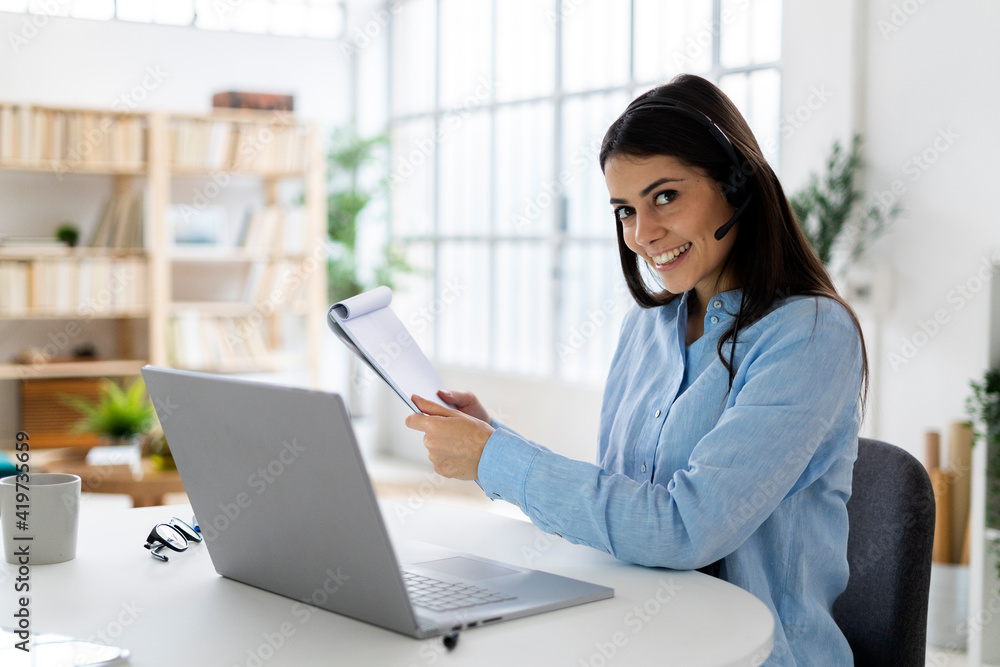 Customer service representative holding note pad while sitting by desk at office Customer service representative holding note pad while sitting by desk at office