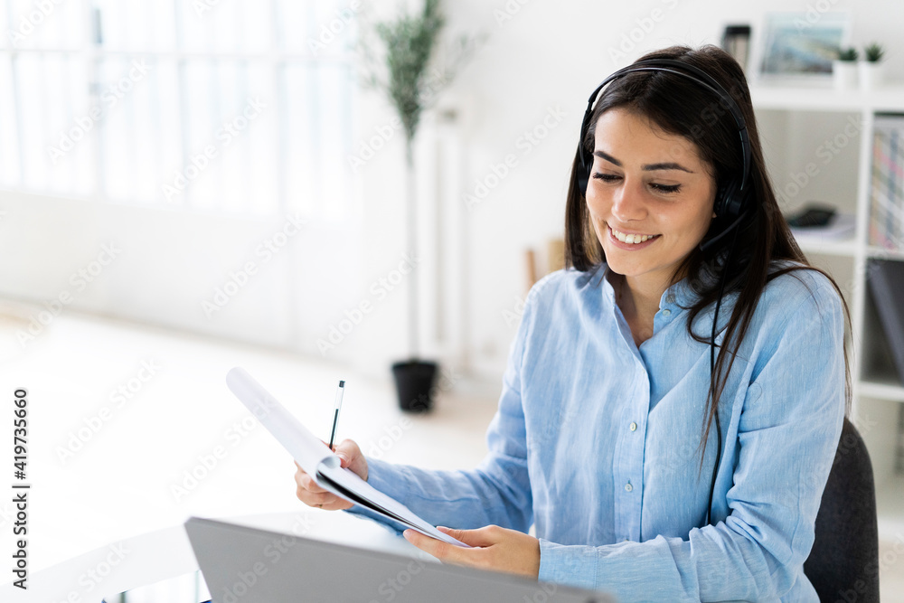 Professional wearing microphone headset smiling while working on laptop at office Professional wearing microphone headset smiling while working on laptop at office