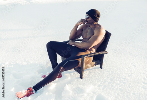 Thoughtful shirtless sportsman looking away while sitting on chair in snow photo