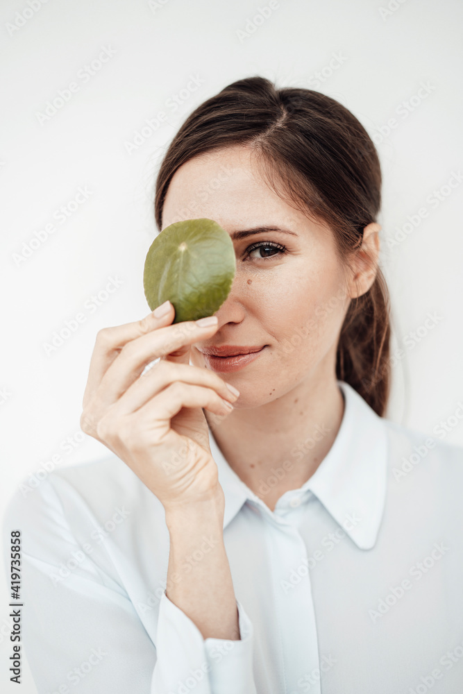 Elegant businesswoman holding leaf on her eye against white background in studio Elegant businesswoman holding leaf on her eye against white background in studio
