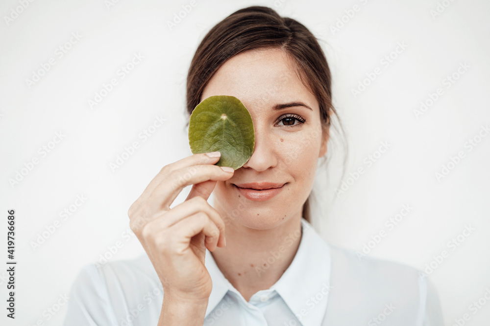 Businesswoman holding leaf on her eye against white background in studio Businesswoman holding leaf on her eye against white background in studio