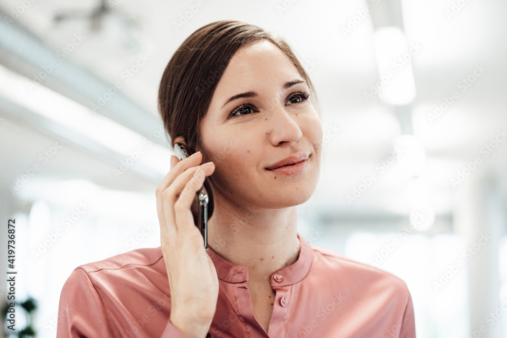 Smiling businesswoman looking away while talking on smart phone at office Smiling businesswoman looking away while talking on smart phone at office