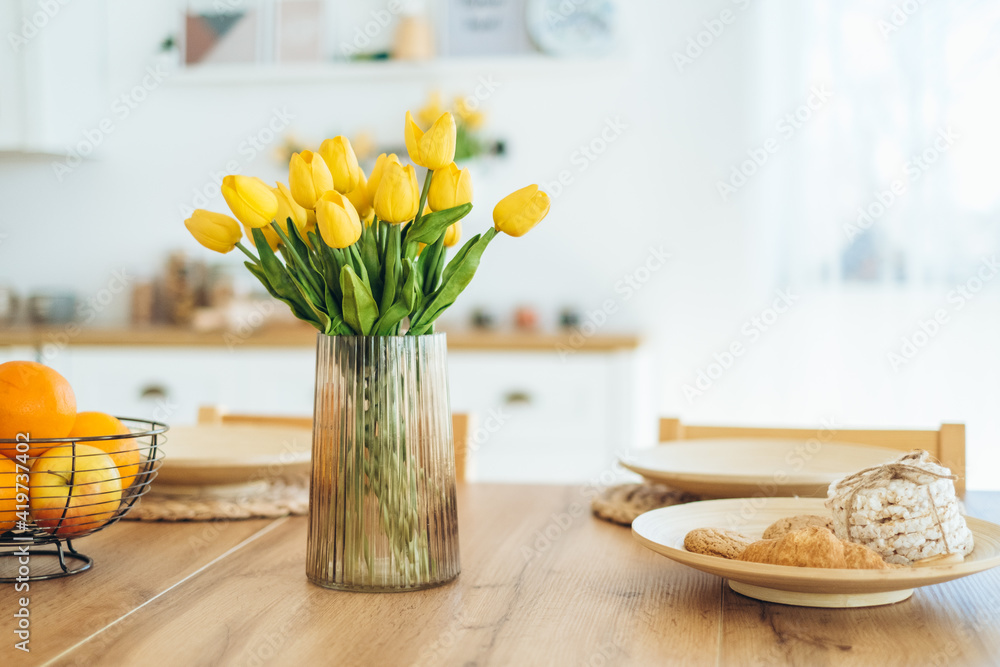 Yellow tulips in a vase on the table. Spring holiday, Easter, home decor. - obrazy, fototapety, plakaty 