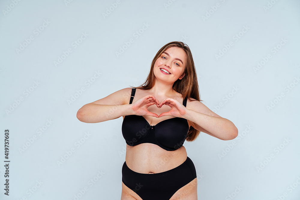 Curvy young woman wearing black bikini gesturing heart shape against white background Curvy young woman wearing black bikini gesturing heart shape against white background