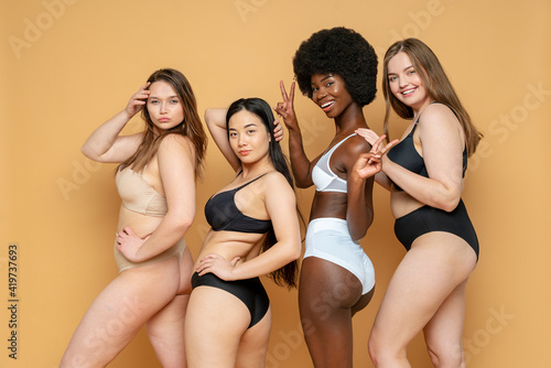 Confident young women in lingerie standing against yellow background photo