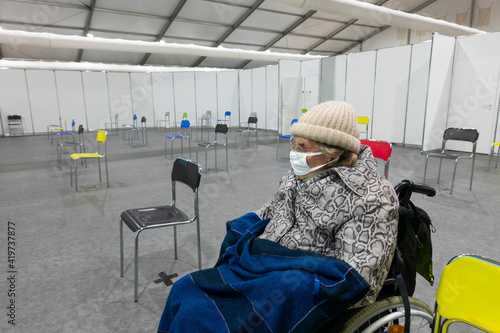 Senior women wearing protective face mask and warm clothing sitting on wheelchair at vaccination center photo