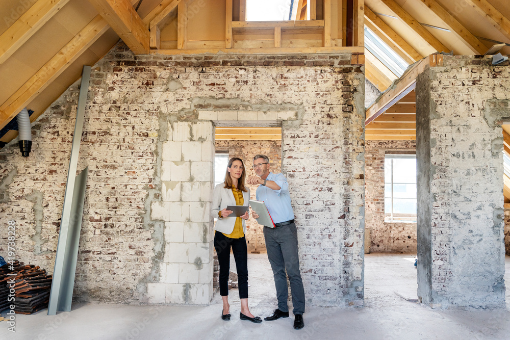 Architect explaining to businesswoman standing with digital tablet at construction site Architect explaining to businesswoman standing with digital tablet at construction site