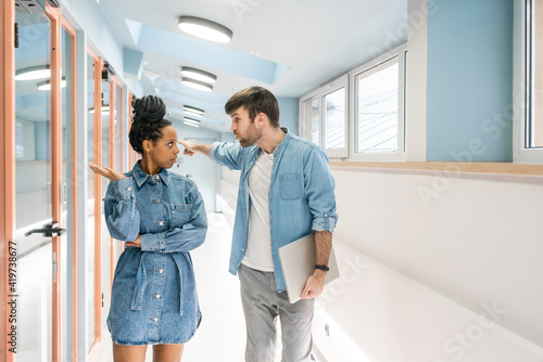 Businessman arguing with female colleague while standing in office corridor photo