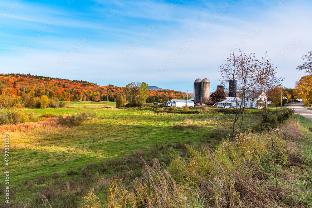 Rural landscape in Vermont with farm buildings along an unpaved road on a sunny autumn day. Stunning fall foliage.