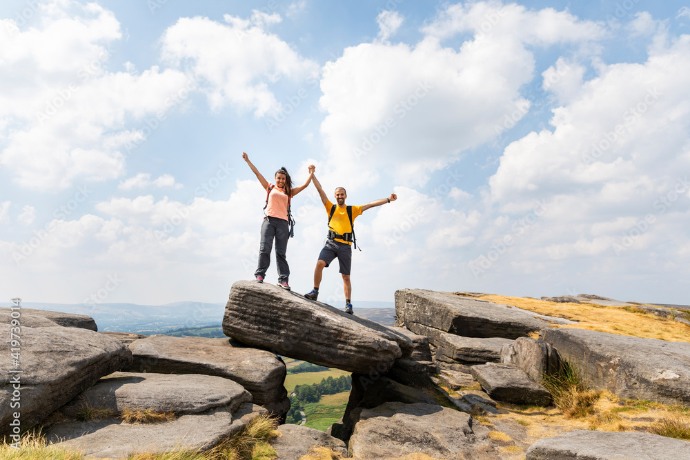 Cheerful friends with arms raised while holding hands on top of mountain against cloudy sky