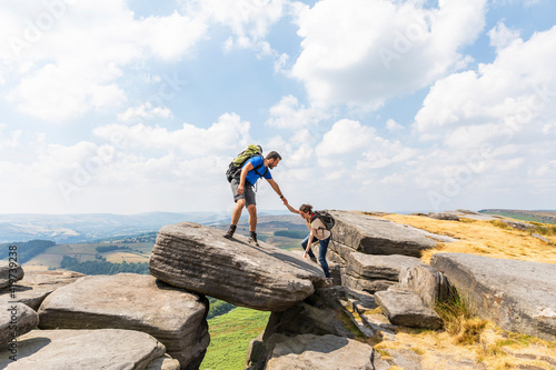 Male hiker helping female friend for climbing mountain during vacations on sunny day