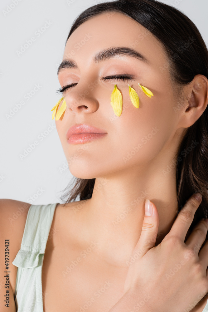 young woman with closed eyes and yellow petals on face isolated on white