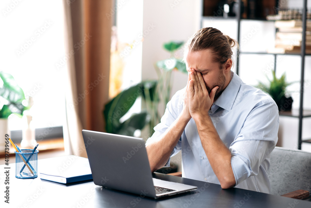 Caucasian unhealthy man feeling bad, sick with running nose, need a rest.Male manager or freelancer sit at the desk at home office, working distantly, using paper tissue, sneezing Caucasian unhealthy man feeling bad, sick with running nose, need a rest.Male manager or freelancer sit at the desk at home office, working distantly, using paper tissue, sneezing