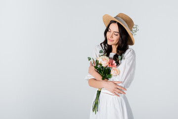 smiling woman in straw hat and dress holding bouquet of spring flowers isolated on white