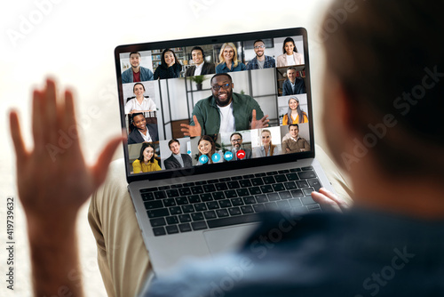 Online video communication concept. Over shoulder view at a laptop screen with different people, employees, business partners, guy greets colleagues, online briefing, brainstorming, group teleworking
