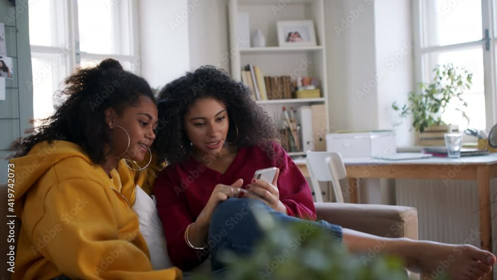 Portrait of young sisters with smartphone indoors at home, laughing. Portrait of young sisters with smartphone indoors at home, laughing.