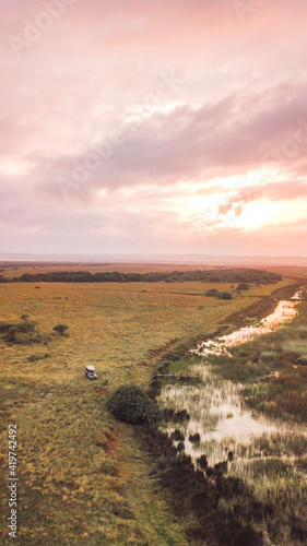 A landscape of South Africa with a pink sunset sky with a car in the filed