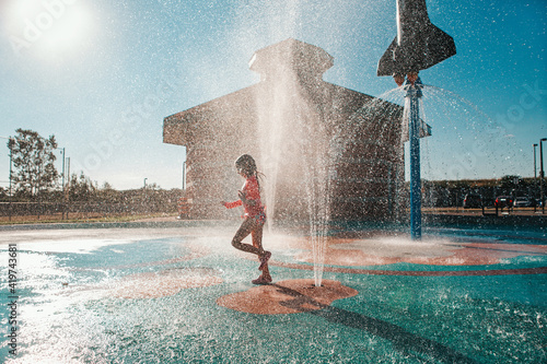 Cute adorable Caucasian funny girl playing on splash pad playground on summer day. Seasonal water sport recreational activity for kids outdoors.