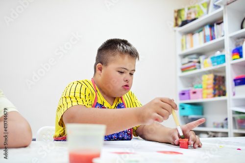 Boy with Down syndrome draw at a table on a white background