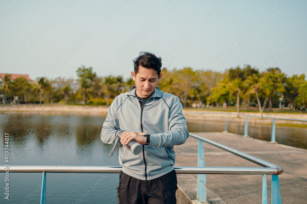 Happy sport man in earphone listen music standing and checking at smartwatch during training and running in the park.