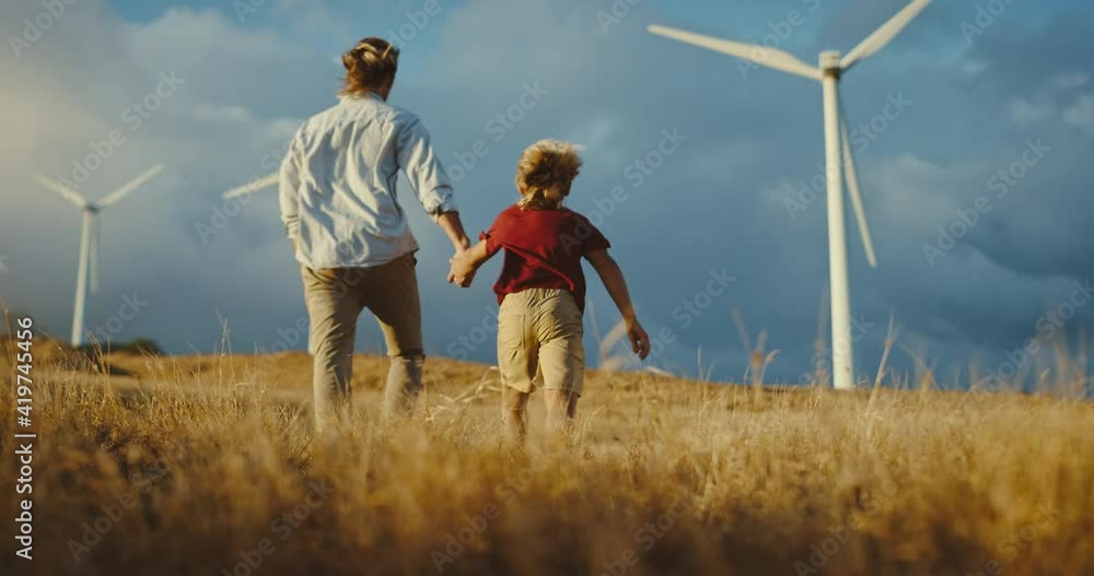 Father and son walking to windmills on golden hill at sunset, family lifestyle, clean energy wind turbines, future generations and clean sustainable energy Father and son walking to windmills on golden hill at sunset, family lifestyle, clean energy wind turbines, future generations and clean sustainable energy