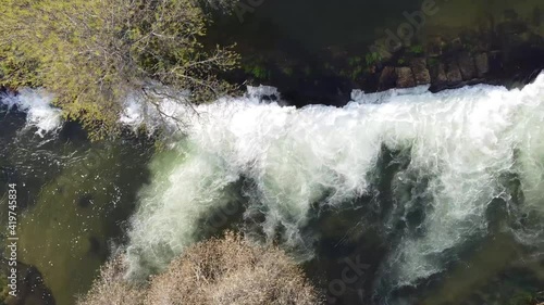 drone running across the width of a small and beautiful waterfall. At the end you can see a suspension bridge photo