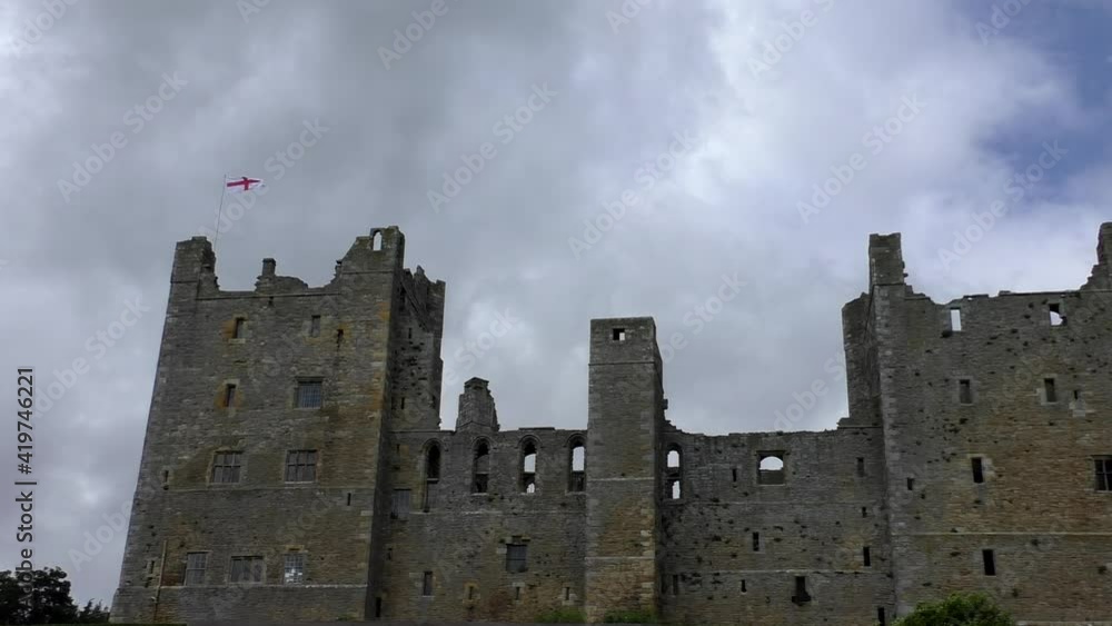 Low angle view of St George's flag of England flying above castle, clouds floating in the sky. Low angle view of St George's flag of England flying above castle, clouds floating in the sky.