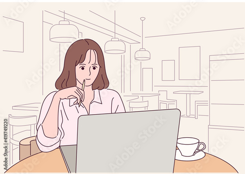 A woman is sitting in a cafe and working on a laptop.