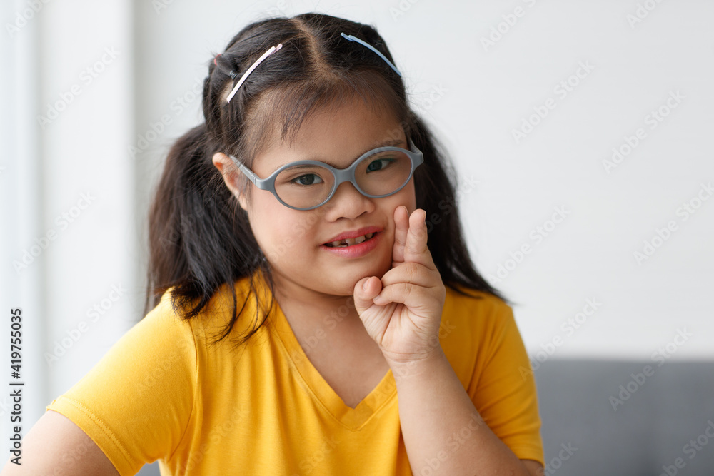 Portrait of a young down syndrome girl wearing eyeglasses in beautiful and colorful clothes looking at camera with a self-confident and wildly open smile with happiness. Idea for happy disabled kid Portrait of a young down syndrome girl wearing eyeglasses in beautiful and colorful clothes looking at camera with a self-confident and wildly open smile with happiness. Idea for happy disabled kid