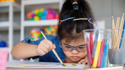 Young Asian down syndrome little girl sitting at desk with colors and painting with concentrated and calm. painting. Concept for education for disabled kid