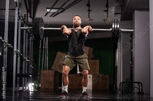 Muscular athlete lifting very heavy barbell