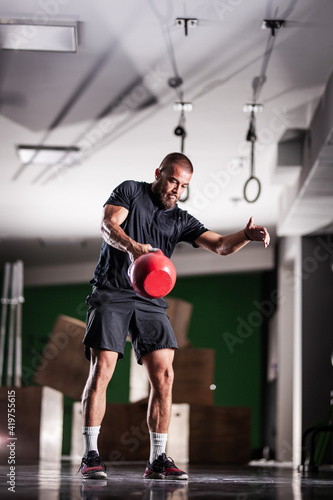 Muscular athlete power lifting a kettlebell. Man working out indoors