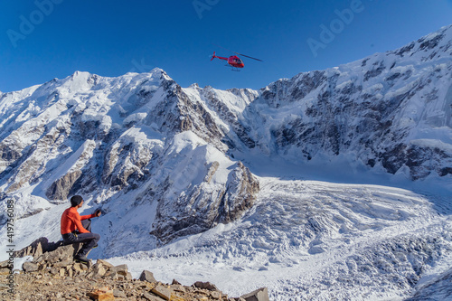 A beautiful landscape with mountains, a huge blue glacier and a middle-aged mountaineer sitting with a walkie-talkie in his hands calls the rescue service waiting for an ambulance helicopter