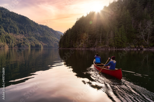 Couple friends canoeing on a wooden canoe during a colorful sunny sunset. Cloudy Sky Artistic Render. Taken in Harrison River, East of Vancouver, British Columbia, Canada.