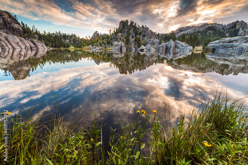 dramatic summer sunrise with the sky and clouds reflecting on the still Sylvan Lake in the Black Hills of South Dakota.