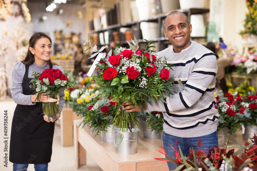 Experienced woman florist helping male client to choose flowers in flower shop