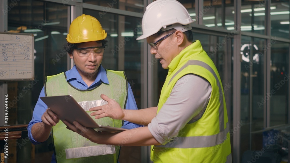 Two factory industrial workers technician or engineer and manager wear uniforms safety feeling upset with the engine machine of the factory arguing about planning procedure of work on laptop computer Two factory industrial workers technician or engineer and manager wear uniforms safety feeling upset with the engine machine of the factory arguing about planning procedure of work on laptop computer