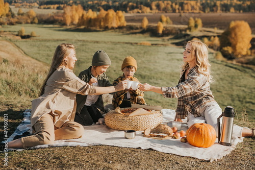 big unconventional family having a picnic in a beautiful place in nature. two women and 2 boys are drinking tea and eating pizza, resting on the street. 