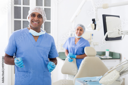 Portrait of professional male dentist in office with dental assistant background