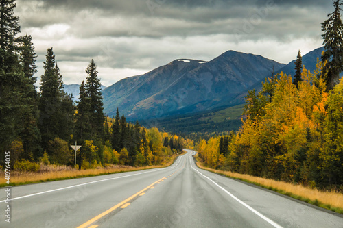 road trip on open highways traversing jagged snow capped mountain peaks and vibrant autumn foliage of the trees in wild Alaska.