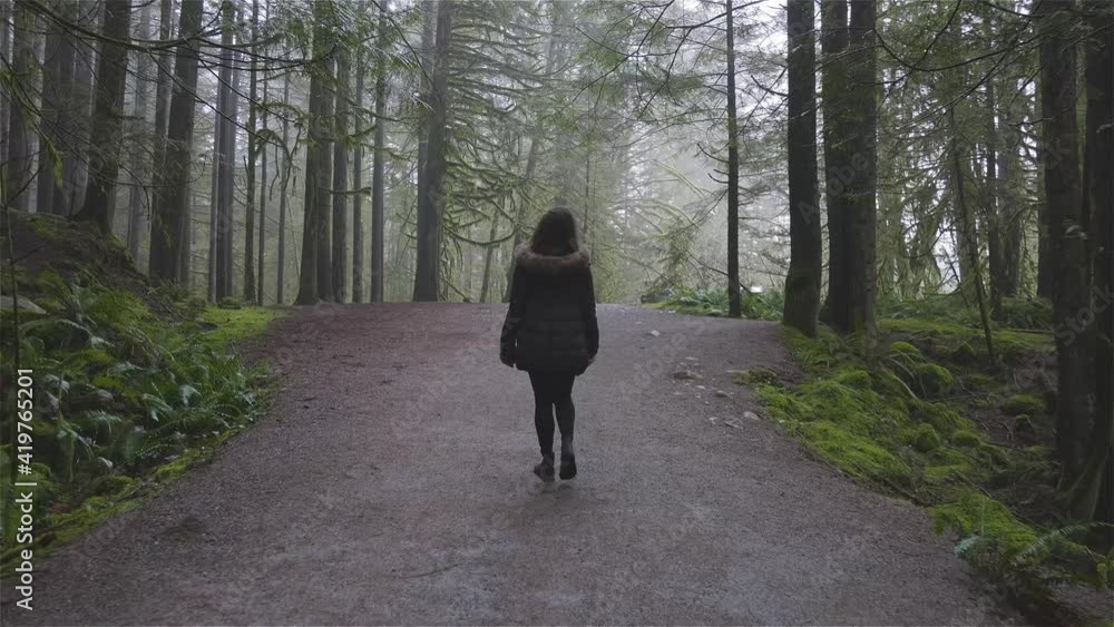 Girl Walking on a Beautiful Path in the Rainforest during a wet and rainy day. Lynn Canyon Park, North Vancouver, British Columbia, Canada. Girl Walking on a Beautiful Path in the Rainforest during a wet and rainy day. Lynn Canyon Park, North Vancouver, British Columbia, Canada.